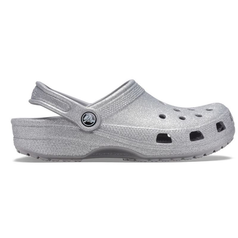 Crocs Classic Glitter Clog 205942 so udobni in lahki natikači z bleščečim glitter dizajnom, ki združujejo prepoznavno Crocs udobje in moderen, izrazit videz. Izdelani iz Croslite™ materiala zagotavljajo mehko blaženje, vodoodpornost in enostavno čiščenje, zato so primerni za vsakodnevno nošenje in modne kombinacije.