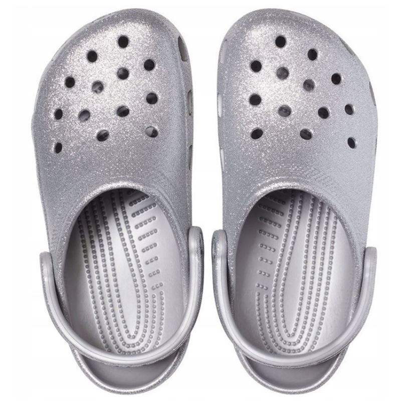 Crocs Classic Glitter Clog 205942 so udobni in lahki natikači z bleščečim glitter dizajnom, ki združujejo prepoznavno Crocs udobje in moderen, izrazit videz. Izdelani iz Croslite™ materiala zagotavljajo mehko blaženje, vodoodpornost in enostavno čiščenje, zato so primerni za vsakodnevno nošenje in modne kombinacije.