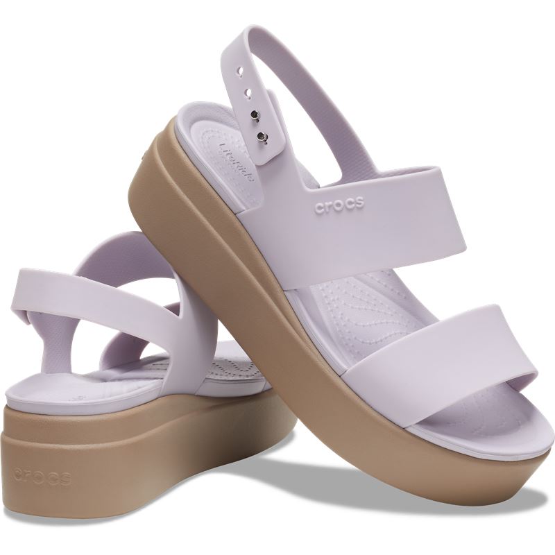 Ženski sandali Crocs Brooklyn Low Wedge W 206453 z elegantno nizko polno peto, lahkotno zasnovo in udobnimi paščki za moderen poletni videz.